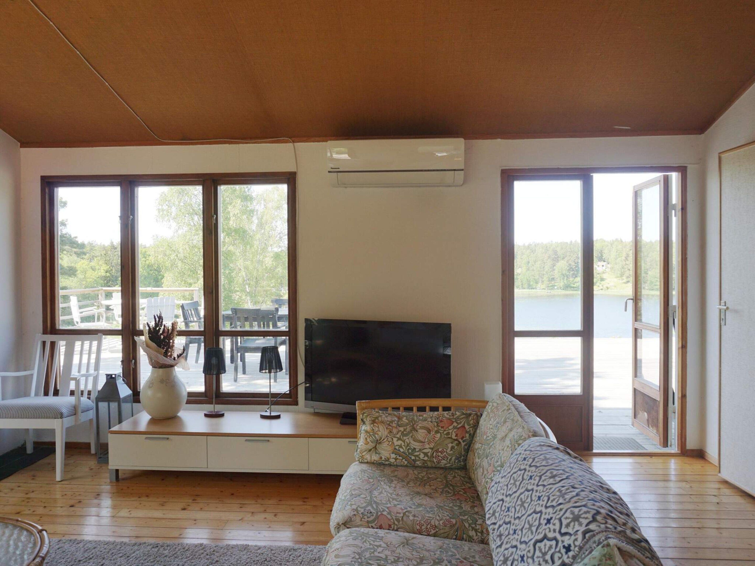Sala de estar com sofá, televisão e uma grande janela com vista para um deck.