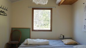 Quarto com duas camas, uma janela, uma cadeira e uma luminária fixada na parede.