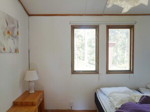 Ein Schlafzimmer mit zwei Fenstern, einem Nachttisch mit Lampe und einem Bett mit lila Decke.