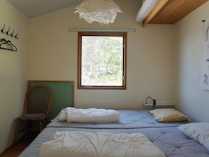A bedroom with a bed, a chair, a window, and a wall-mounted light fixture.
