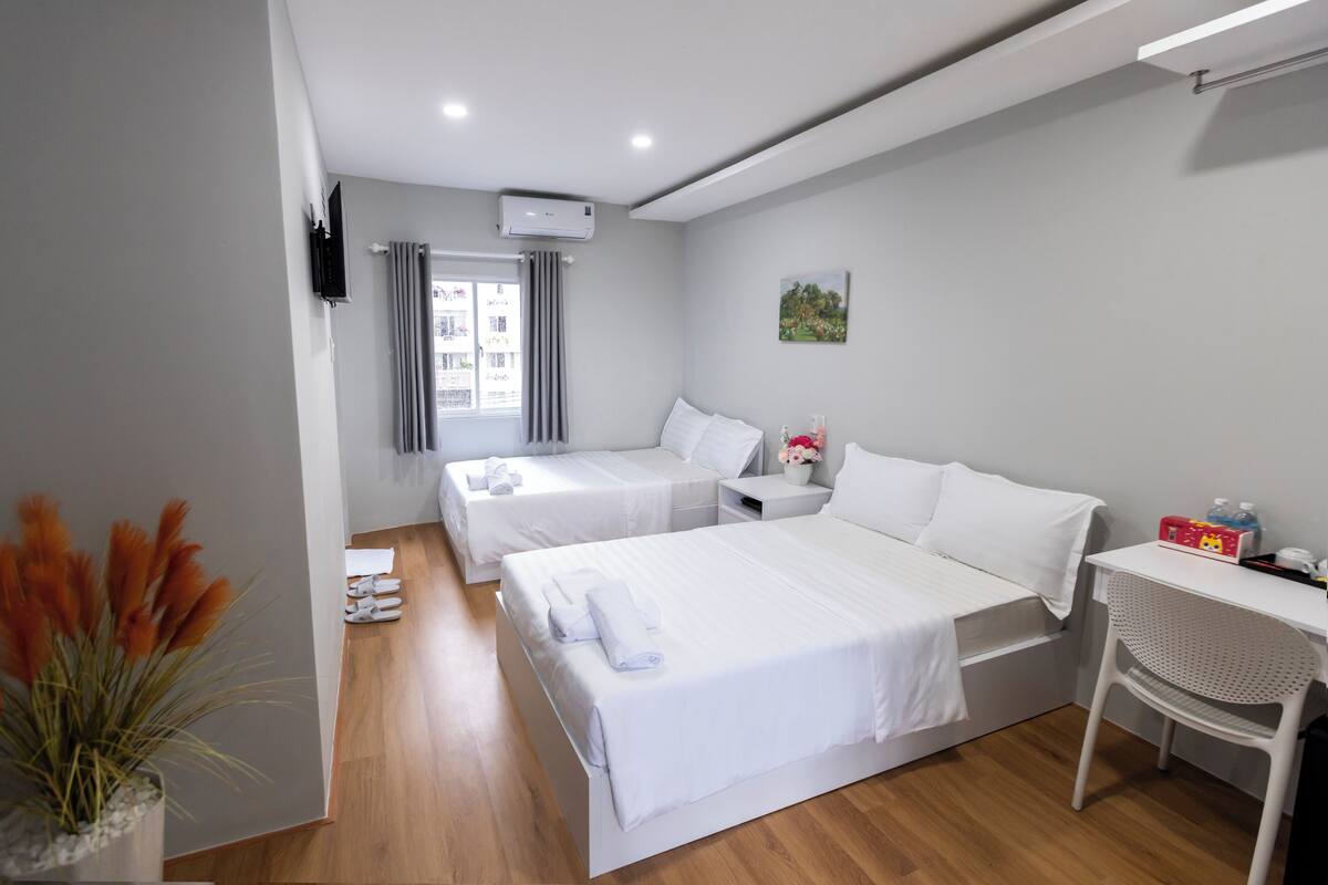 A hotel room with two beds, a desk, a chair, a TV, and a window with curtains.