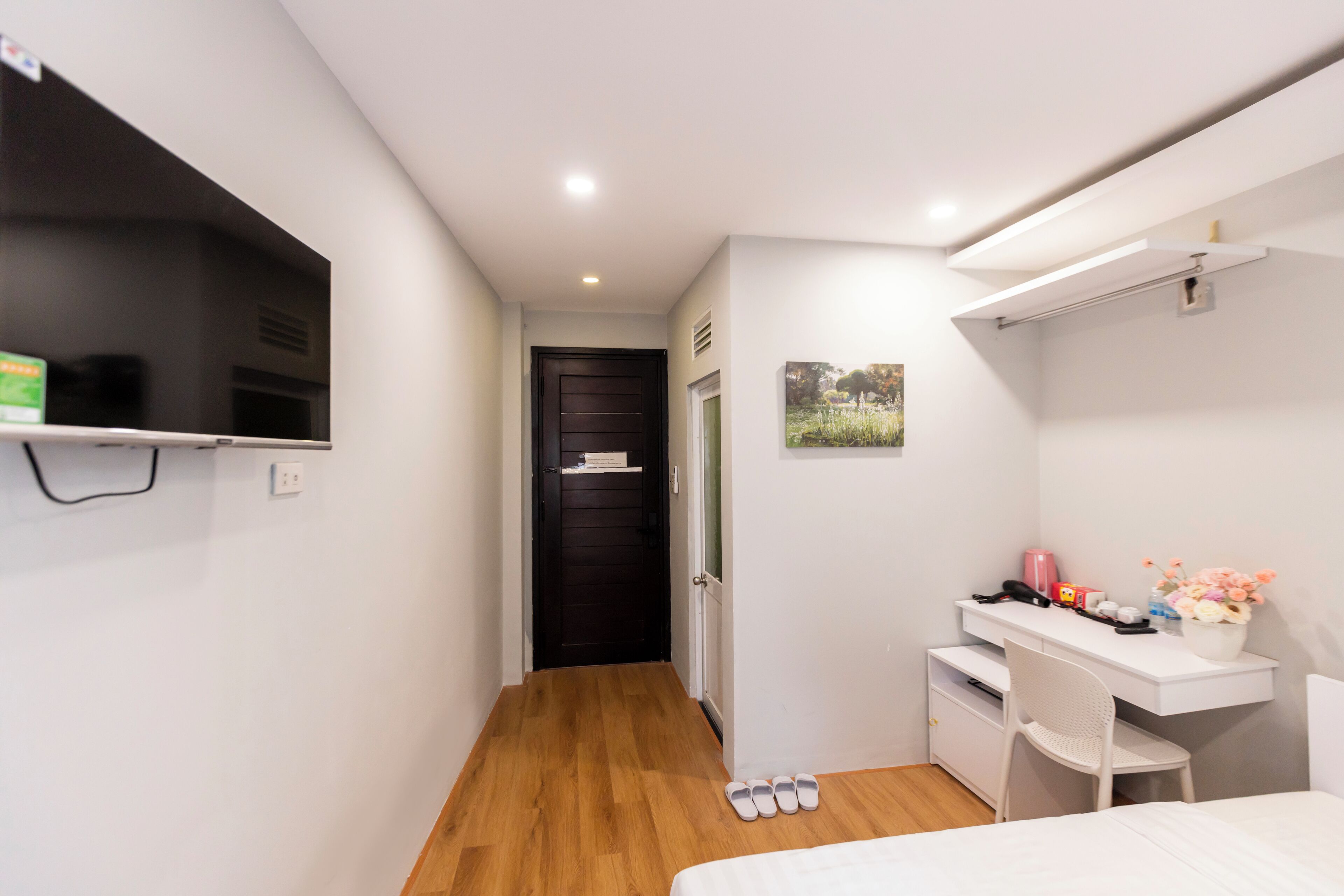A compact bedroom with a bed, a desk, and a TV mounted on the wall.