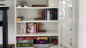 A white bookshelf with multiple shelves containing books, board games, and decorative items.