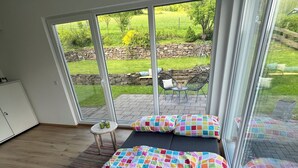 A bedroom with a large window, a bed with a colorful quilt, and a view of a garden.