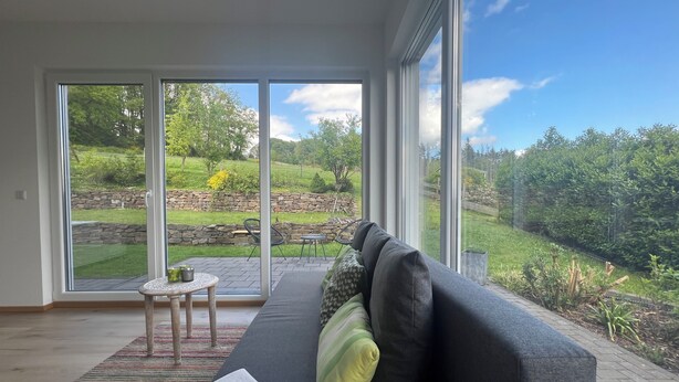 A modern living room with a large sliding glass door leading to a garden.