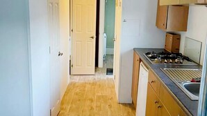 Una cocina estrecha con armarios de madera, una estufa a gas y un refrigerador pequeño.