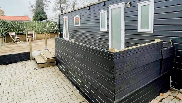 Una casa móvil compacta de color oscuro con una pequeña terraza y dos ventanas.