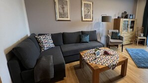 A modern living room with a dark grey sofa, two framed artworks on the wall, a wooden coffee table, and a blue rug. - Holiday Apartment Alleblas (Geldern)