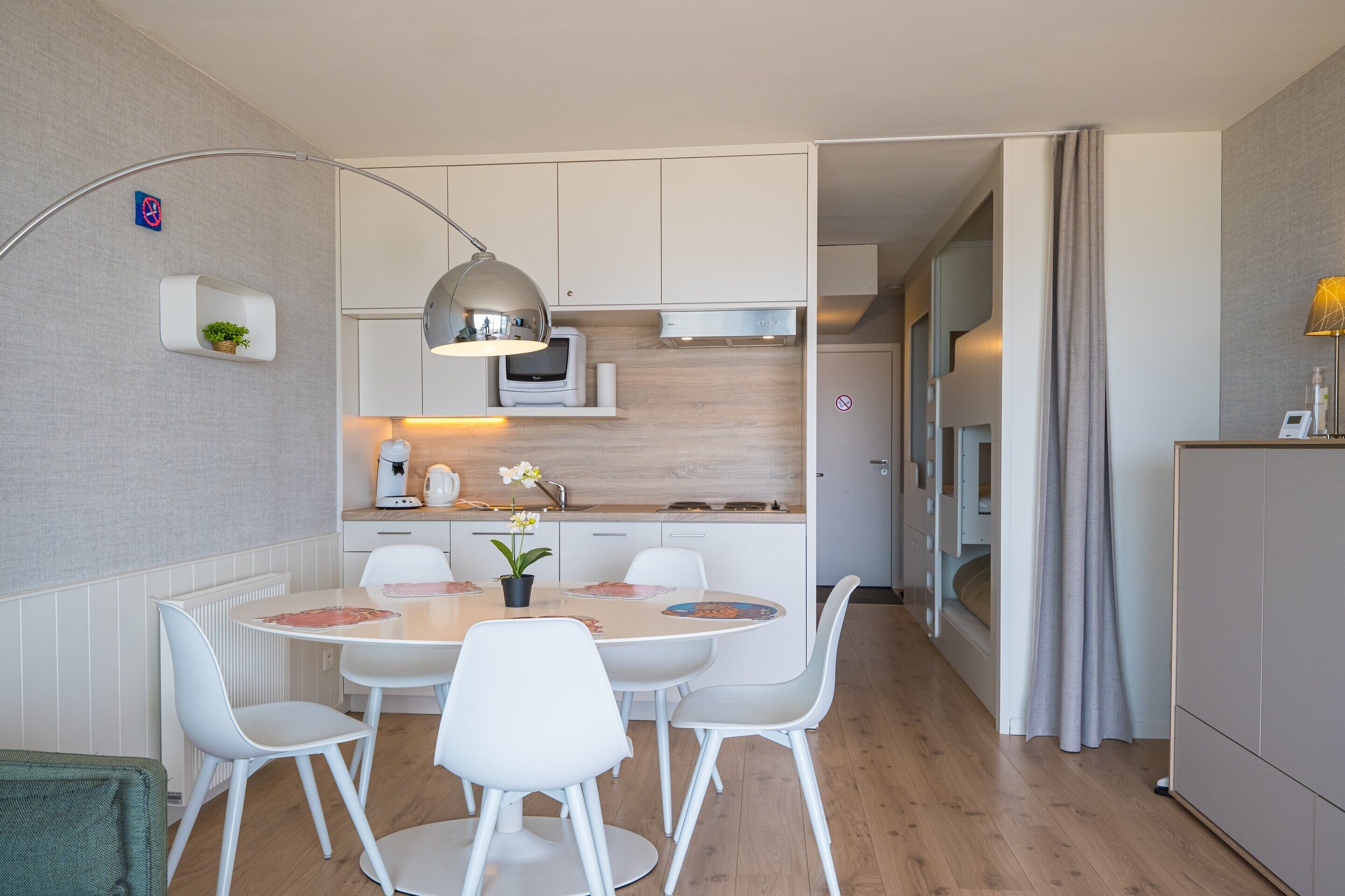 A modern kitchen with white cabinets, a built-in microwave, and a dining area with white chairs and a round table.