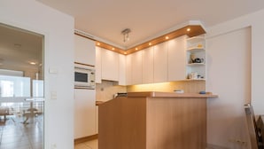 A modern kitchen with a central island, white cabinetry, and a built-in microwave. - Apartment in Nieuwpoort by the Seafront (Koksijde)