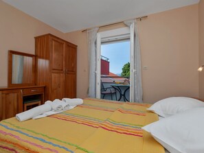 A bedroom with a bed, a wooden wardrobe, a small table with chairs, and a balcony with a table and chairs. - Apartments Villa Juric - One Bedroom Apartment With Balcony - 4 (Baska Voda)