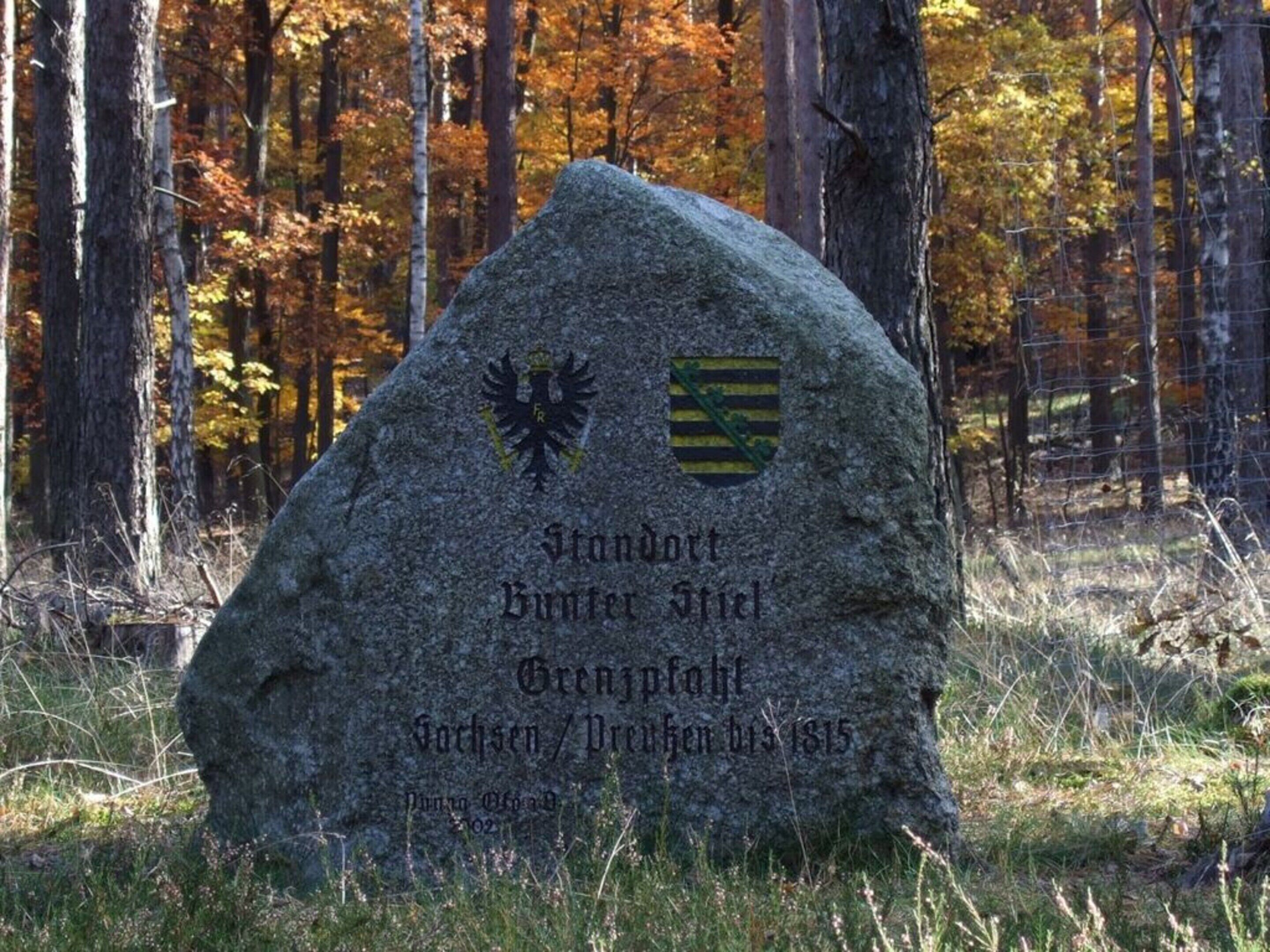 A stone monument with inscriptions and emblems, surrounded by autumn foliage.