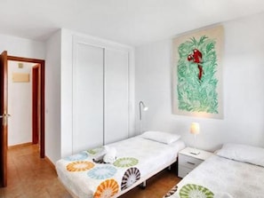 A hotel room with two single beds, a nightstand, a wall-mounted lamp, and a door leading to another room. - Belvilla by OYO Apartment in Guaa de Isora (Guia de Isora)