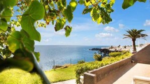A coastal property with a stone wall, a grassy lawn, and a view of the sea.