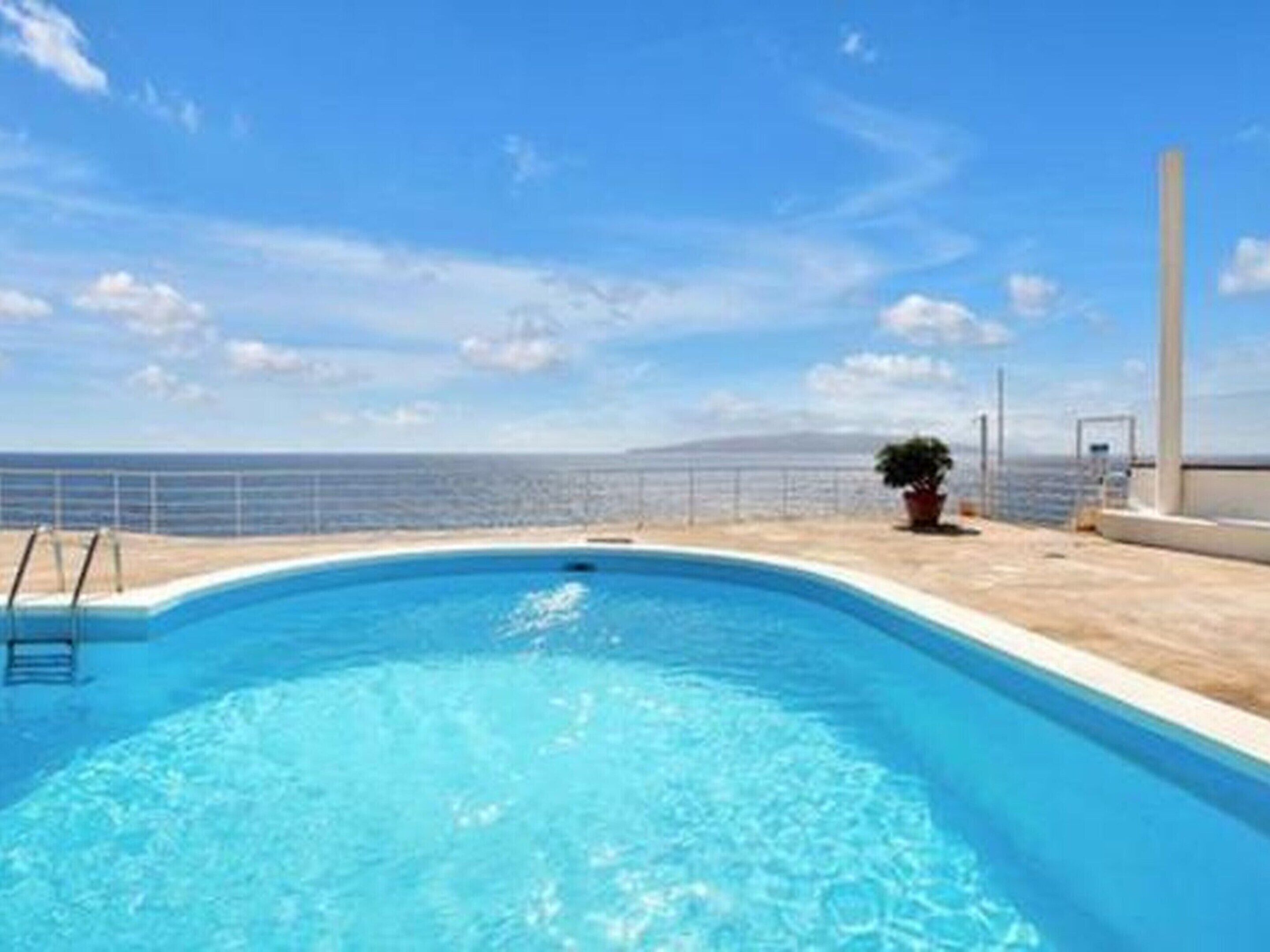 A clear blue swimming pool with a view of the sea and a clear sky.
