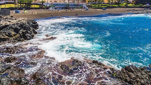 A coastal hotel with a beach view, rocky shoreline, and multiple buildings in the background.