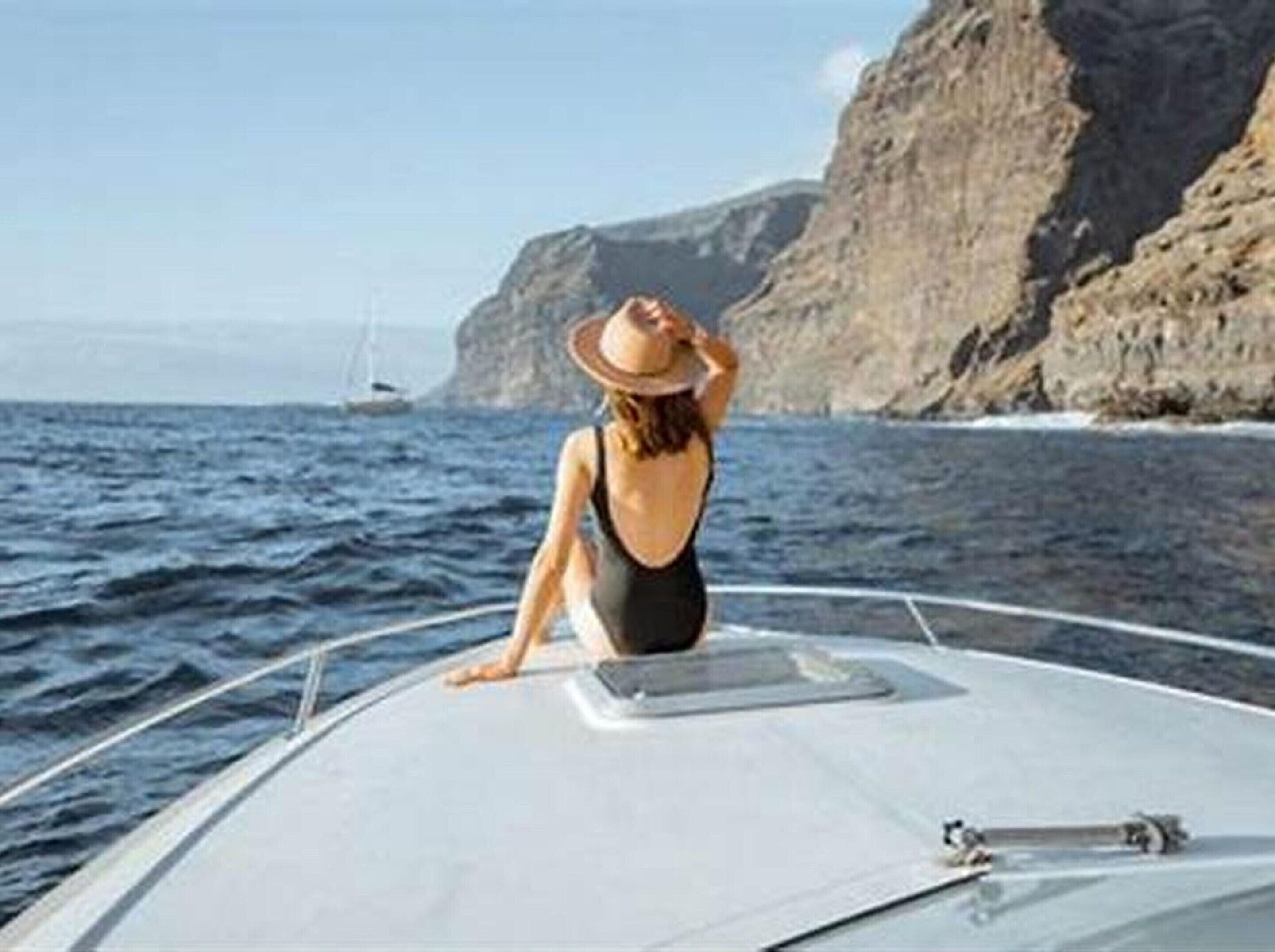 Una persona en un bote frente a un litoral rocoso.