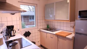 Een kleine keuken met een raam, een magnetron, een spoelbak en een koelkast.