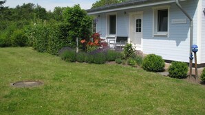 Een gelijkvloers huis met een voortuin, een kleine tuin met verschillende planten en bloemen, en een naambordje op de deur.