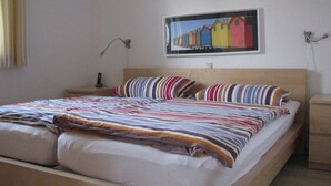 Een bed met een gestreept dekbed en kussens, een nachtkastje met een lamp, en een ingelijst schilderij aan de muur.