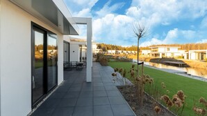 Una casa moderna con un patio, vistas a un río y un bosque al fondo.