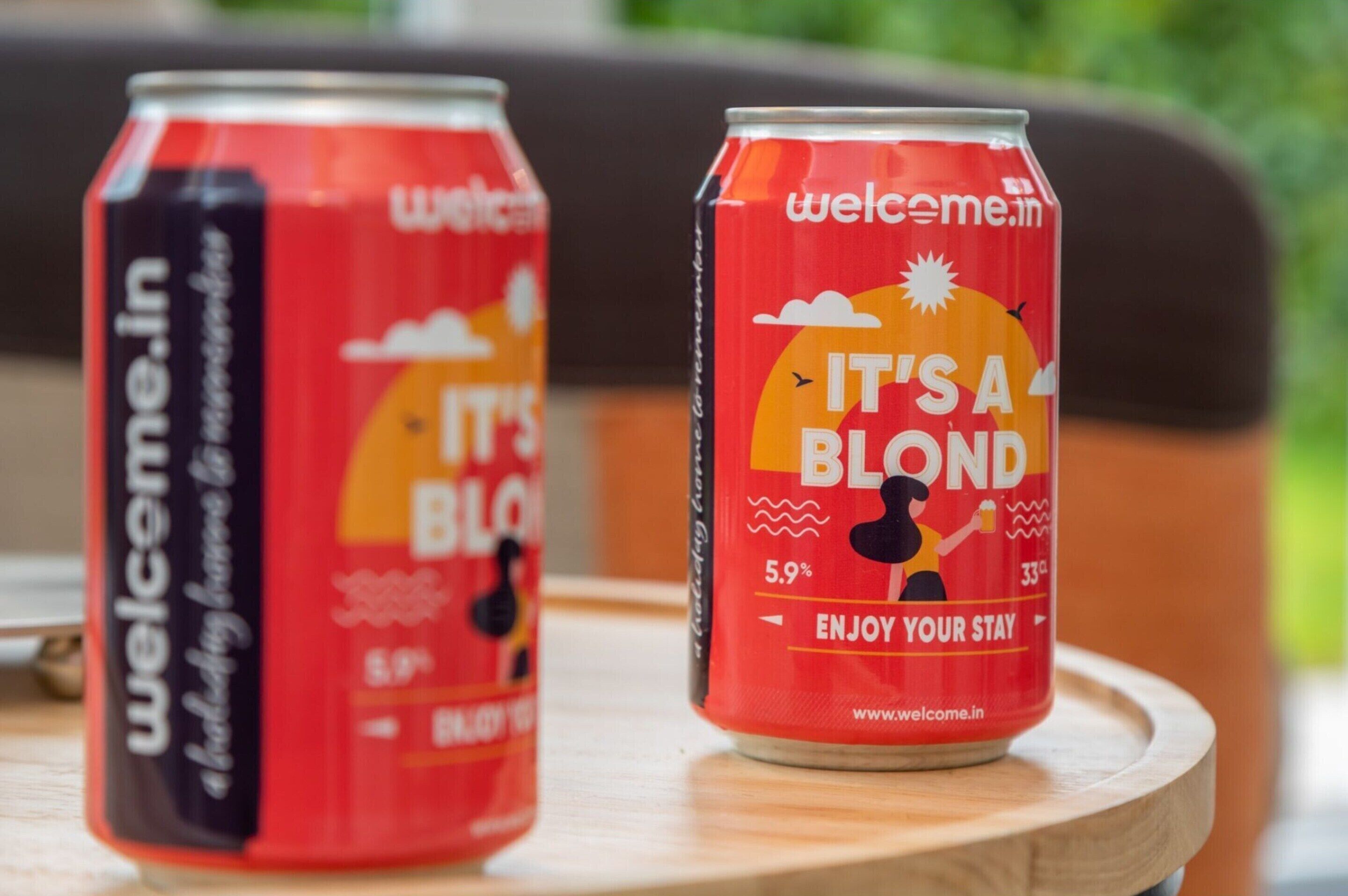 Zwei Dosen des Getränks 'Welcome.in' mit der Aufschrift 'It's a Blond', platziert auf einer Holztischplatte.