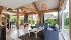 A spacious living area with a large window, a blue sofa, a wooden coffee table, and a TV. - Holiday Home Near Beach Burgh-haamstede (Burgh-Haamstede)