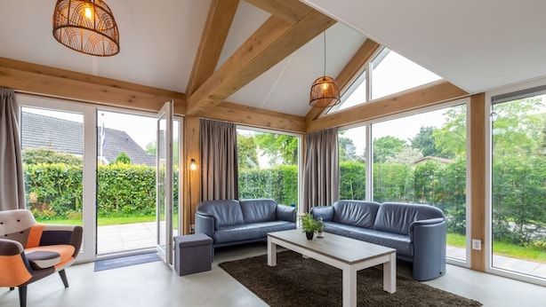 A spacious living room with a modern design, featuring a large sofa set, a coffee table, and a view of the garden through large windows. - Holiday Home Near Beach Burgh-haamstede (Burgh-Haamstede)