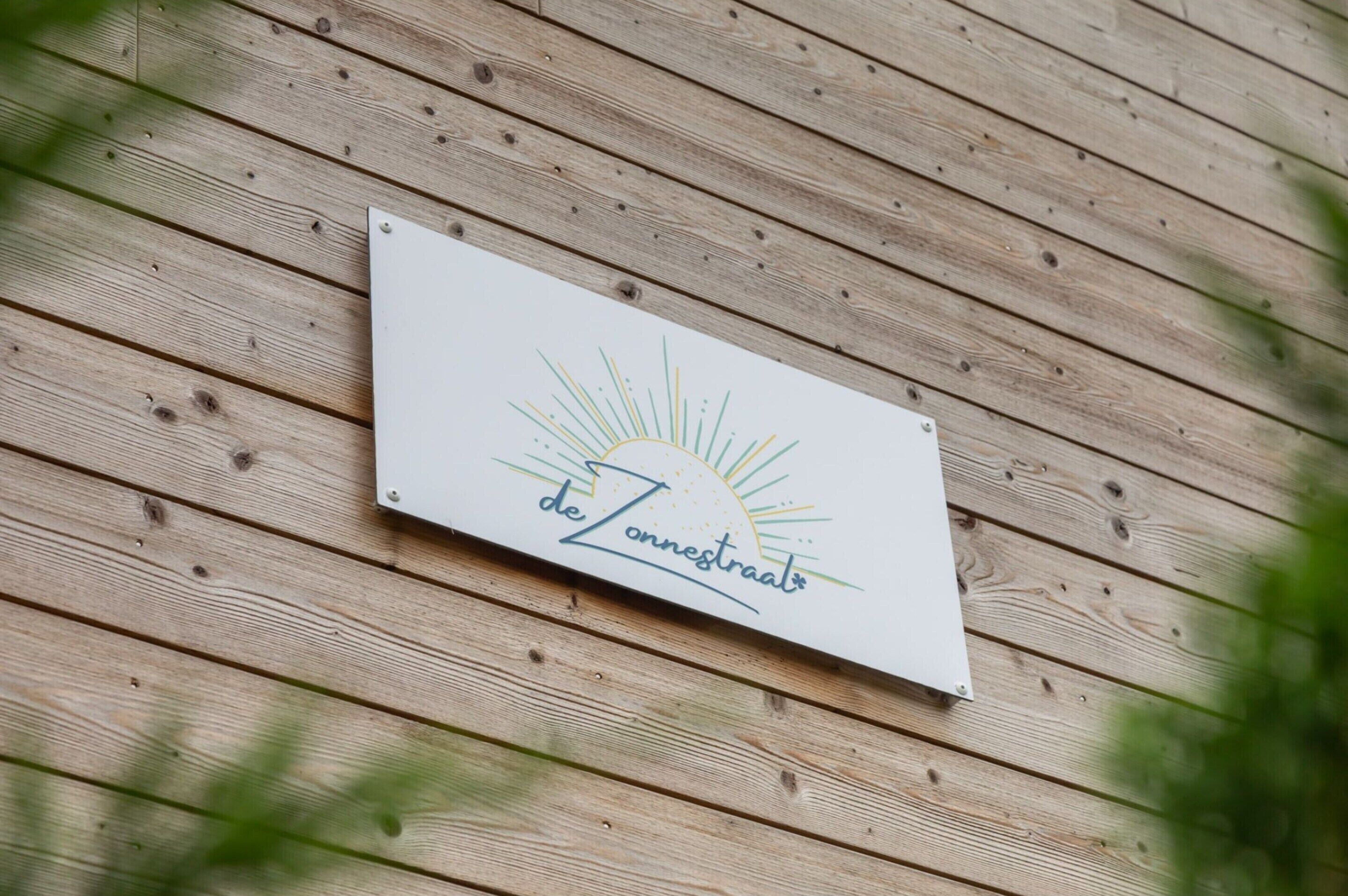 A sign with the text "de Zonnestraal" on a wooden wall.