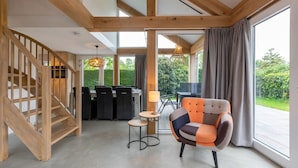 A spacious room with a wooden staircase, a dining area with black chairs, a round table with a lamp, and a colorful armchair. - Holiday Home Near Beach Burgh-haamstede (Burgh-Haamstede)