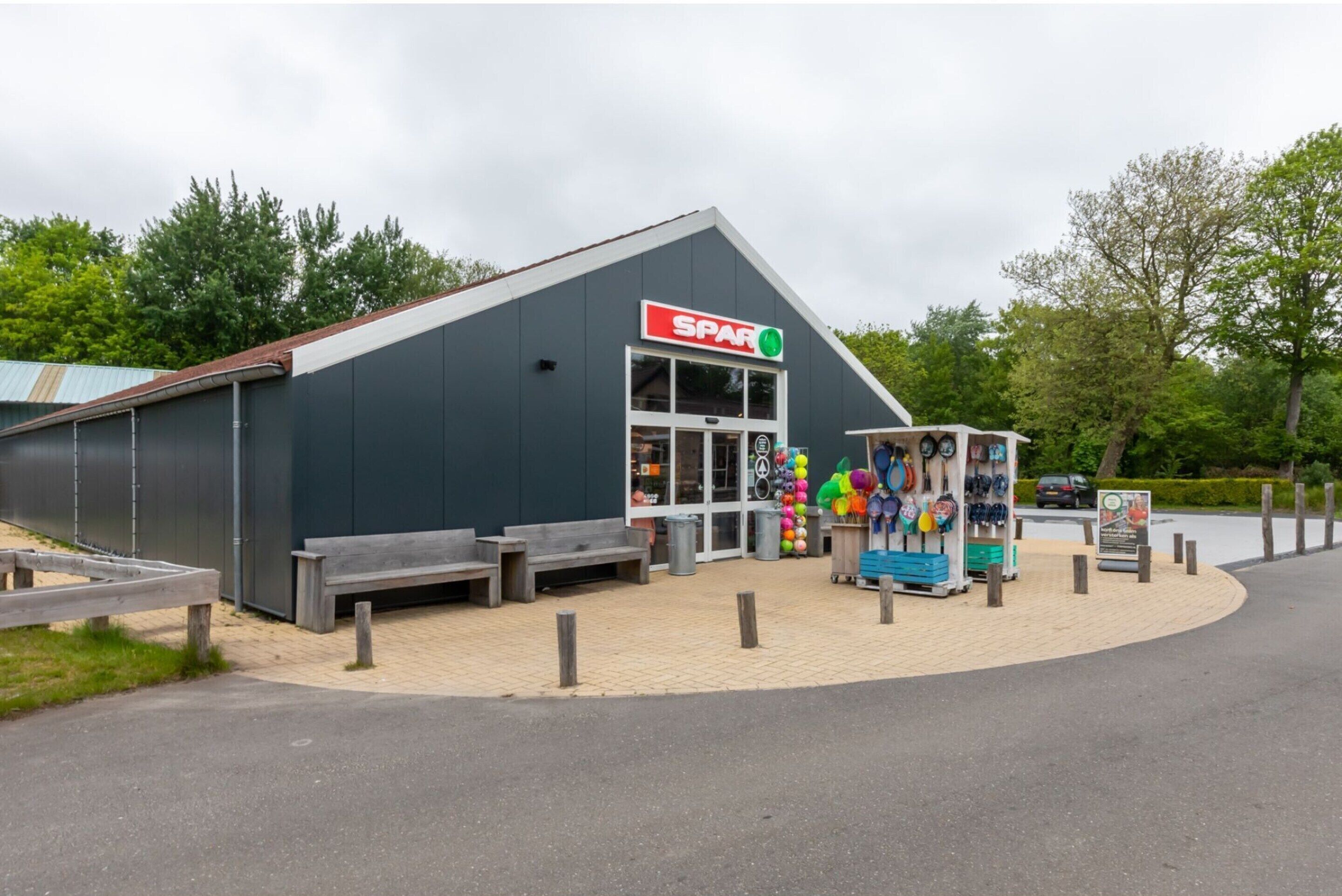 Un bâtiment portant l’enseigne « SPAR », doté d’une terrasse et présentant une variété d’articles colorés.