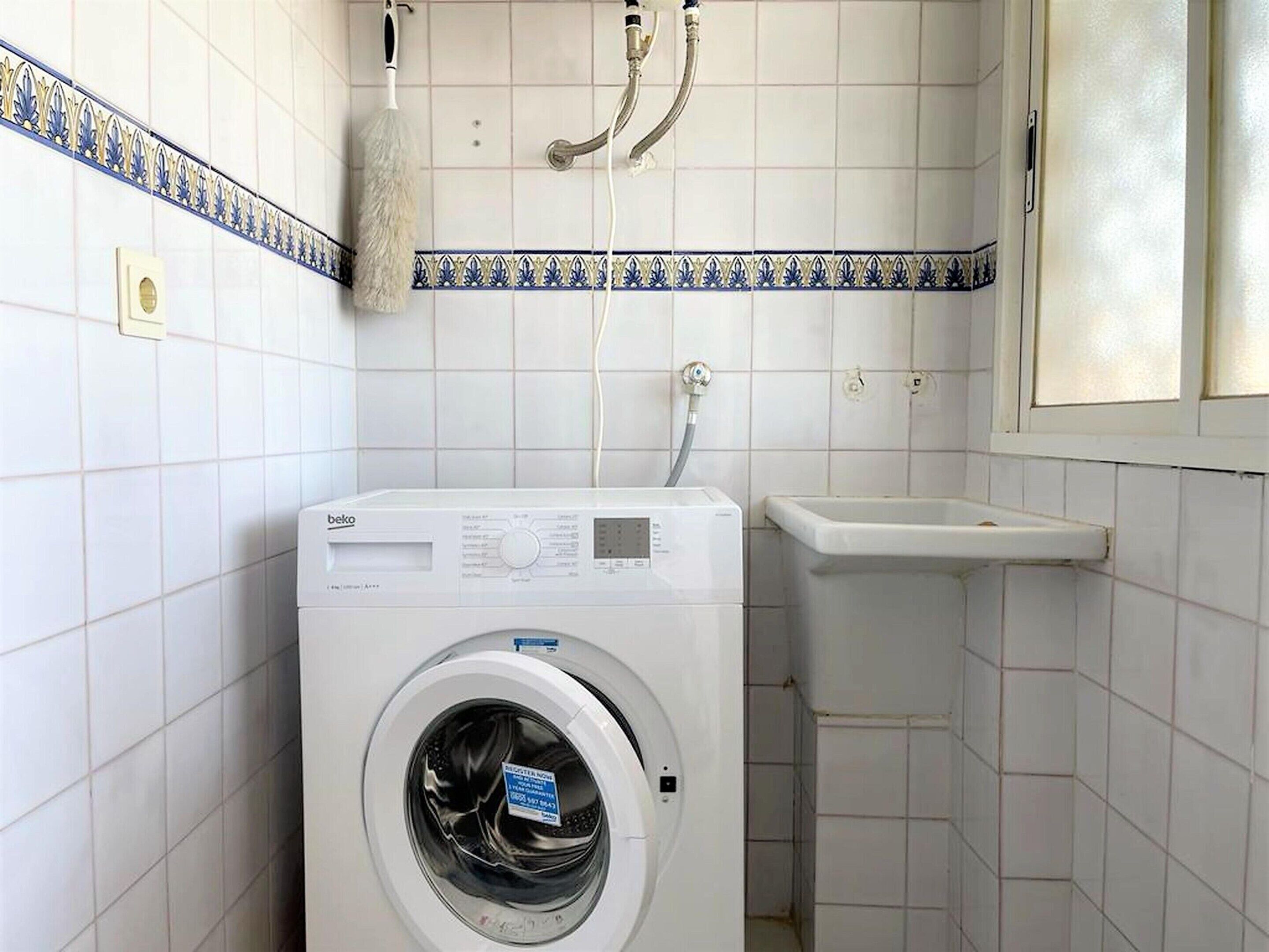 Ein kleiner Waschraum mit einer Waschmaschine mit Frontlader, einem Waschbecken und einer Dusche inklusive Handtuchhalter.