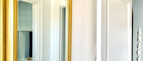 A room with a large mirror, a door, and a wall-mounted light fixture.