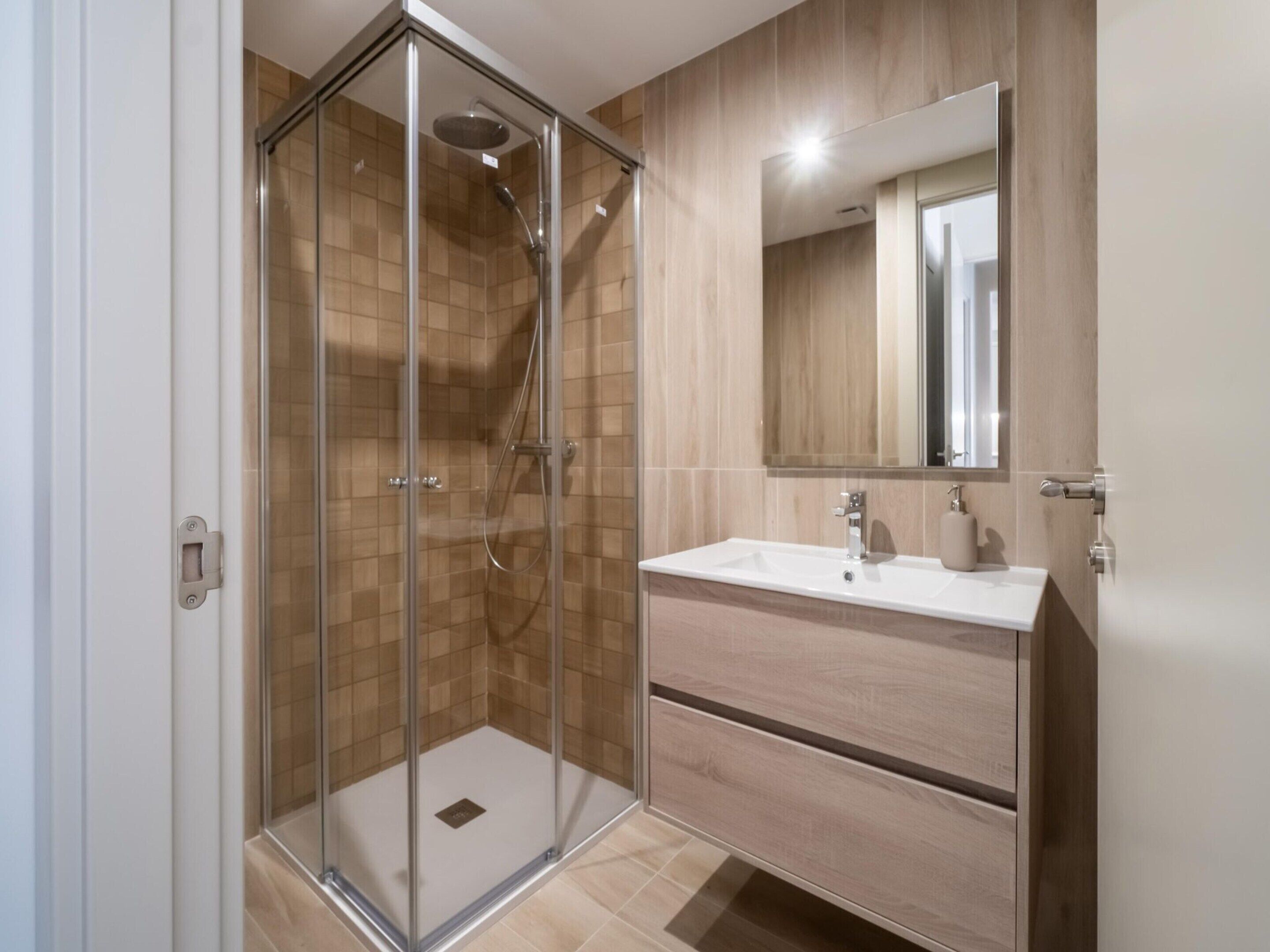 A modern bathroom with a glass-enclosed shower, a white sink, and a wooden vanity.