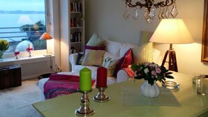 A cozy living room with a bookshelf, a window with a view, a chandelier, and a table with candles and a vase of flowers.