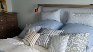 A bed with striped bedding and multiple pillows, a wooden headboard, and a nightstand with drawers.