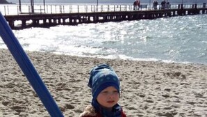 A child standing on a sandy beach with a pier in the background.