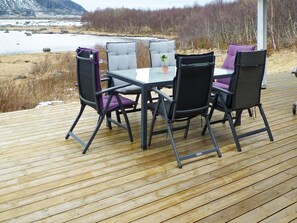 En terrass med ett bord och fyra stolar, med utsikt över en sjö eller ett annat vattendrag och ett skogsområde.