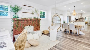A modern living room with a brick fireplace, white walls, and a dining area with a chandelier.