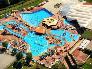 Vista aérea de un complejo turístico con varias piscinas, tumbonas, sombrillas y una amplia zona cubierta.