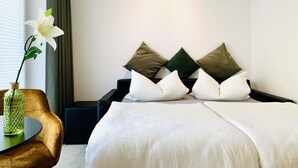 Hotellihuone, jossa on sänky, pieni pöytä maljakko täynnä kukkia ja tuoli.