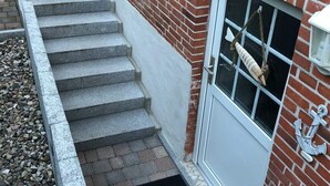 A set of stone steps leading to a door with a window, a brick wall, and a small outdoor area with gravel. - Balticliving Modern Retreat (Timmendorfer Strand)