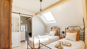 Een slaapkamer met twee bedden, een dakraam, een houten garderobe en uitzicht op de badkamer.