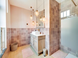 A bathroom with a white sink, wooden cabinet, and a mirror above it. There are two light fixtures hanging from the ceiling, and a trash can is placed near the sink. - Lush Holiday Home in Limburg With Jacuzzi (Bree)