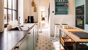 Een moderne keuken met een groot raam, een koffieapparaat, een spoelbak en een blauwgroene inbouwkast boven het aanrecht.