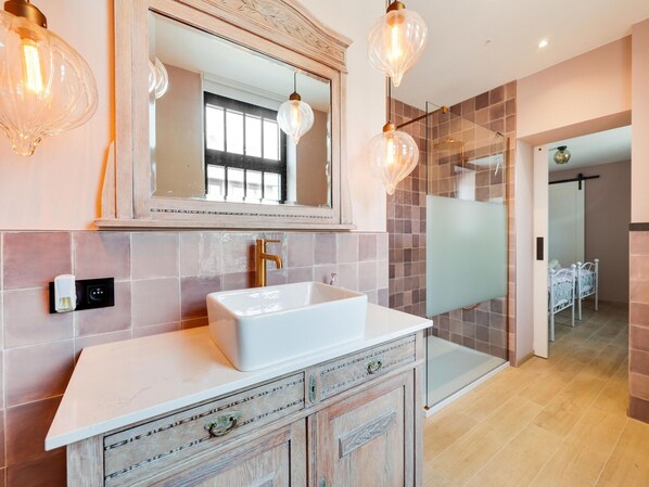 Un baño moderno con lavamanos blanco, un espejo grande y una cabina de ducha de vidrio.