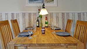 A wooden dining table with four chairs, a framed coastal landscape picture above, and a bottle of champagne on the table. - Holiday Apartment "kati" (Lancken-Granitz)