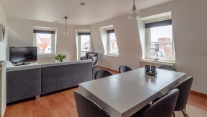 Un appartement moderne comprenant une cuisine, un coin repas et un salon. De nombreuses fenêtres offrent une vue sur la ville.