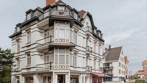 Un immeuble à plusieurs étages, avec une entrée d’angle, des balcons et un commerce situé au rez-de-chaussée.