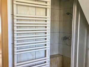 Ein Badezimmer mit weißem Handtuchhalter, gefliesten Wänden und einer Duschkabine.